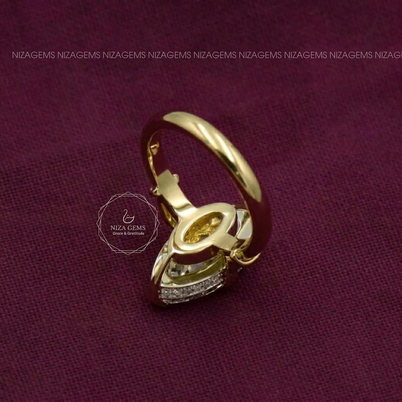 May include: A gold ring featuring a central marquise-cut gemstone and a band accented with small pav&eacute;-set diamonds. The ring displays the NIZA GEMS logo and text on the side, with a smooth, polished gold finish throughout the band.