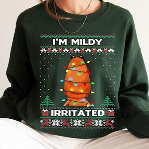 May include: Dark green sweatshirt with the text "I'M MILDY IRRITATED". The graphic features a cartoon potato wrapped in Christmas lights. The design includes festive patterns of snowflakes, trees, and reindeer.
