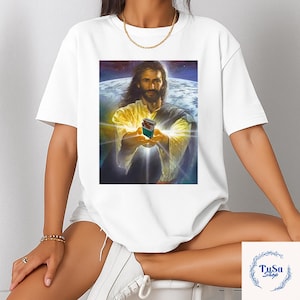 May include: White t-shirt featuring a graphic of Jesus holding a small box with a colorful design against a backdrop of Earth and space. The image has a religious theme.