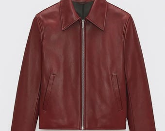 May include: A burgundy leather jacket with a collared neckline and a silver zip. The jacket features two front pockets and long sleeves. The garment is displayed against a white background.