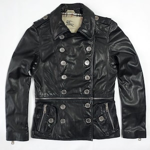 Puede incluir: Chaqueta de cuero negro con diseño de doble botonadura, botones plateados y cierre de cremallera. La chaqueta tiene un cuello clásico, dos bolsillos delanteros con cremalleras y charreteras. El forro interior tiene un estampado a cuadros.