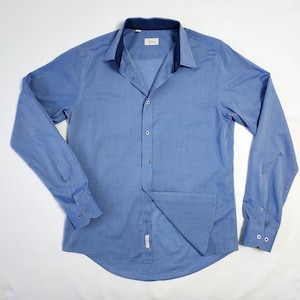 May include: A light blue long-sleeve shirt with a button-down front and a dark blue collar. The shirt has a chest pocket and buttoned cuffs. The brand name is visible on the collar.