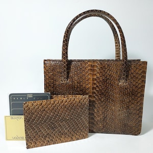 Puede incluir: Un bolso marrón con estampado de piel de serpiente con dos asas, una cartera a juego y un tarjetero. El bolso y la cartera tienen una superficie texturizada. El tarjetero tiene la palabra "Buxton" impresa.