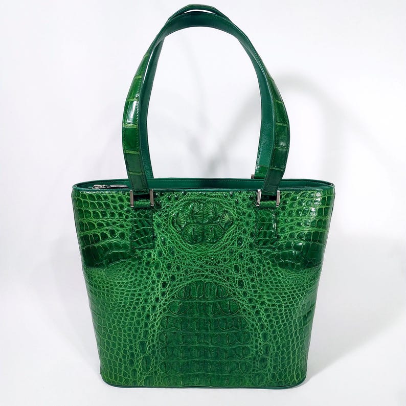 Pu&ograve; includere: Una borsa tote in pelle verde con una texture a pelle di coccodrillo. La borsa ha due manici superiori e una chiusura con cerniera. La borsa &egrave; di una tonalit&agrave; verde vibrante.