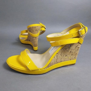 Puede incluir: Sandalias de cuña amarillas brillantes con detalles de corcho. Las sandalias presentan un acabado brillante en las correas y la plataforma, con cierre de hebilla en la correa del tobillo. El tacón de cuña proporciona soporte y estilo.