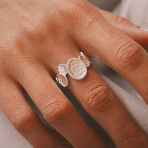 May include: A silver bracelet and ring set featuring a series of circular, textured elements. The bracelet is composed of multiple connected discs, while the ring has a cluster of smaller, similar discs. The jewelry is displayed on a hand.