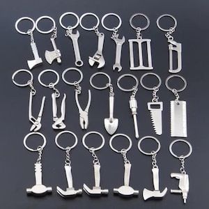 Könnte beinhalten: Eine Sammlung von silberfarbenen Metallschlüsselanhängern, die jeweils mit einem Miniatur-Werkzeuganhänger versehen sind. Das Set enthält verschiedene Utensilien wie eine Axt, Schraubenschlüssel, Zangen, eine Schaufel, einen Schraubendreher, eine Säge, ein Lineal, Hämmer und eine Bohrmaschine, die alle an runden Ringen befestigt sind.