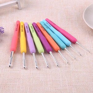 May include: A set of eight crochet hooks with colorful silicone handles in pink, yellow, lavender, light green, purple, orange, light blue, and cyan. Each hook features a silver metal tip and is printed with its specific size, ranging from 3/0 to 10/0.