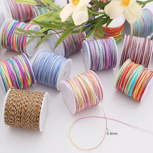 Puede incluir: Múltiples carretes de cordón de nailon de colores para manualidades, cada uno con un patrón de rayas multicolor distinto. Un carrete muestra un hilo extendido hacia afuera con el texto 0.8mm impreso cerca, indicando el grosor del cordón.