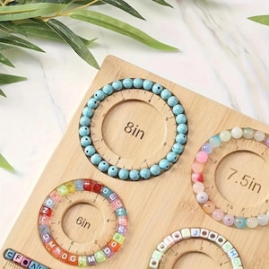May include: A wooden bead board featuring circular cutouts with printed measurements of 6 inches, 7.5 inches, and 8 inches. The board holds a turquoise stone bead bracelet, a multi-colored letter bead bracelet, and a pastel bead bracelet.