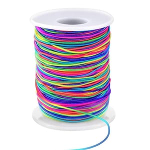 Könnte beinhalten: Eine Spule mit elastischer Kordel in einem leuchtenden Regenbogen aus Farben, darunter Neonpink, leuchtendes Gelb, Limettengrün, Elektroblau und Violett. Die Kordel ist fest um eine weiße, zylindrische Kunststoffspule mit einem Mittelloch gewickelt.