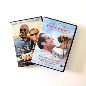 May include: Two DVD cases featuring movie cover art. One case displays The Bucket List with Morgan Freeman and Jack Nicholson. The other case shows As Good As It Gets with Jack Nicholson, Helen Hunt, and Greg Kinnear, featuring a small brown dog.