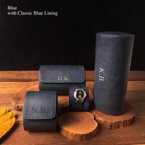 Pode incluir: Um conjunto de estojos de relógio de couro azul e um relógio com pulseira verde. Os estojos são de várias formas e tamanhos, alguns com iniciais gravadas. O texto "Blue with Classic Blue Lining" está no topo.