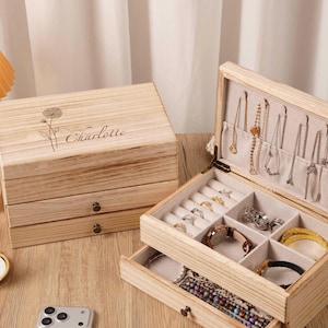 May include: Wooden jewellery box with multiple compartments and drawers. The box is open, revealing rings, bracelets, and necklaces. The lid is engraved with a floral design and the name "Charlotte".
