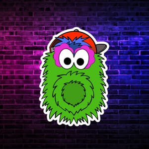 May include: A cartoon character sticker with a green, furry body, large black eyes, and pink eye accents. It wears a red baseball cap with a gray brim and blue hair. The sticker is against a brick wall with pink and blue neon lighting.
