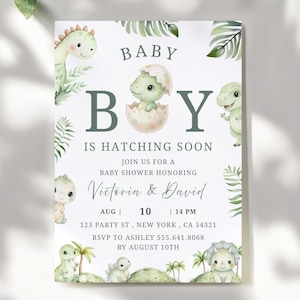 May include: Baby shower invitation with a dinosaur theme. The invitation features a light green and white color scheme with illustrations of baby dinosaurs and tropical leaves. Text includes "Baby Boy is Hatching Soon".
