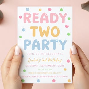 Könnte beinhalten: Eine Geburtstagseinladung mit den Worten "READY TWO PARTY" in Buchstabenblasen. Die Einladung enthält Details für Isabels 2. Geburtstag am 9. September 2025, von 15:00 bis 18:00 Uhr. Die Einladung wird von zwei Händen gehalten.