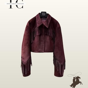 Może przedstawiać: Bordowa zamszowa kurtka z frędzlami na rękawach i piersi. Kurtka ma kołnierz i klasyczny styl western. Logo marki "Impeccable Couture" jest widoczne w lewym górnym rogu.