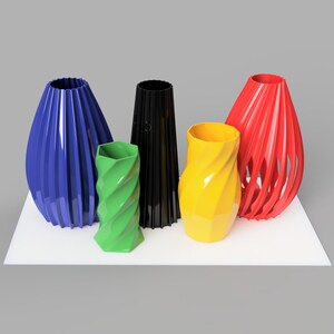 Pode incluir: Uma cole&ccedil;&atilde;o de cinco vasos coloridos em v&aacute;rias formas. Os vasos s&atilde;o em tons de azul, verde, preto, amarelo e vermelho. Est&atilde;o dispostos sobre uma superf&iacute;cie branca contra um fundo cinza. Medidas em cent&iacute;metros.