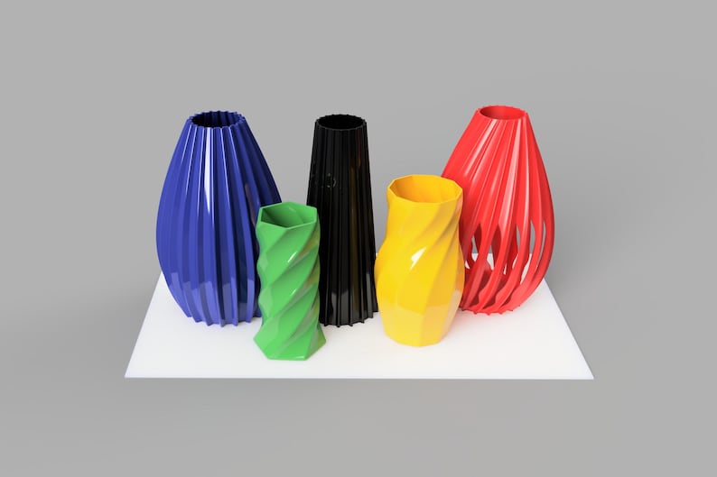 Pode incluir: Uma cole&ccedil;&atilde;o de cinco vasos coloridos em v&aacute;rias formas. Os vasos s&atilde;o em tons de azul, verde, preto, amarelo e vermelho. Est&atilde;o dispostos sobre uma superf&iacute;cie branca contra um fundo cinza. Medidas em cent&iacute;metros.