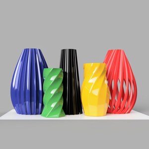 Pode incluir: Um conjunto de cinco vasos coloridos. Os vasos s&atilde;o azuis, verdes, pretos, amarelos e vermelhos. O vaso azul tem ranhuras verticais, o verde tem um design torcido e o vermelho tem um padr&atilde;o aberto, semelhante a uma treli&ccedil;a.