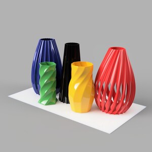Pode incluir: Uma cole&ccedil;&atilde;o de vasos decorativos em v&aacute;rias cores, incluindo azul, verde, preto, amarelo e vermelho. Os vasos t&ecirc;m designs &uacute;nicos, alguns com um padr&atilde;o em espiral ou de ripas abertas. Est&atilde;o dispostos sobre uma superf&iacute;cie branca.
