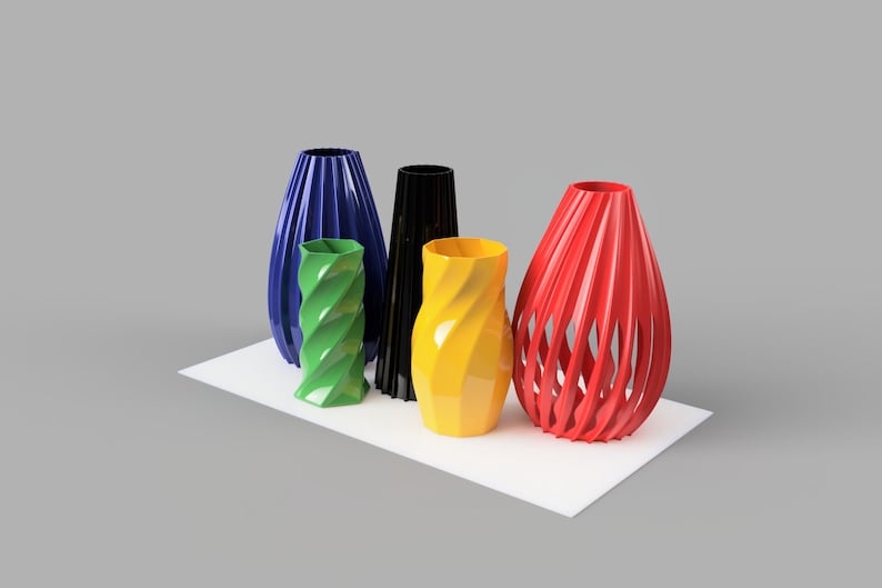 Pode incluir: Uma cole&ccedil;&atilde;o de vasos decorativos em v&aacute;rias cores, incluindo azul, verde, preto, amarelo e vermelho. Os vasos t&ecirc;m designs &uacute;nicos, alguns com um padr&atilde;o em espiral ou de ripas abertas. Est&atilde;o dispostos sobre uma superf&iacute;cie branca.