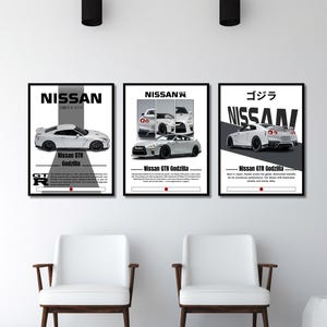 May include: Three framed posters featuring white Nissan GTR Godzilla cars. Each poster has a black frame and includes the Nissan logo and car specifications. The posters are displayed above two white chairs.