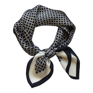 May include: A black and white silk scarf with a repeating chain link pattern. The scarf is knotted and has a cream-coloured border. The scarf is a square shape and is made of a soft, flowing material.