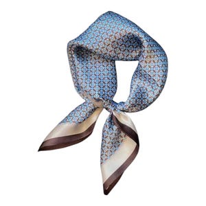 May include: A square silk scarf featuring a geometric design in blue, brown, and cream. The scarf is knotted in the middle, with the ends falling. The edges of the scarf are finished with a dark brown border.