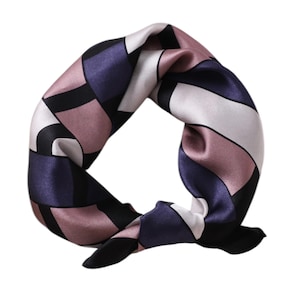 Op de afbeelding: Een vierkante zijden sjaal met een geometrisch patroon. De sjaal heeft een ontwerp van elkaar kruisende vormen in zwart, wit, mauve en marineblauw. De sjaal is geknoopt en wordt tegen een witte achtergrond getoond.