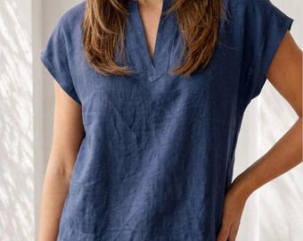 May include: A dark blue short-sleeved top with a V-neckline and a relaxed fit. The garment features a visible textured fabric and a logo in the upper right corner that reads RVC RAVISHA CREATION. The top is paired with light beige trousers.