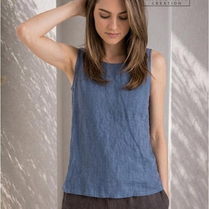 May include: A blue sleeveless top with a round neckline and a textured fabric finish. The garment is paired with dark grey shorts. A logo in the upper right corner displays the text RVC RAVISHA CREATION with a tuxedo icon above the brand name.