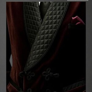 May include: A close-up of a burgundy velvet smoking jacket with a black quilted lapel and black frog closures. The jacket has a pocket with a burgundy lining. The logo "RAVISHA CREATION" is in the upper right corner.