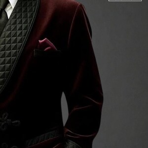 May include: A burgundy velvet blazer with black quilted lapels and cuffs. The blazer features a black tie, a white collared shirt, and a burgundy pocket square. The logo "RAVISHA CREATION" is visible in the upper right corner.
