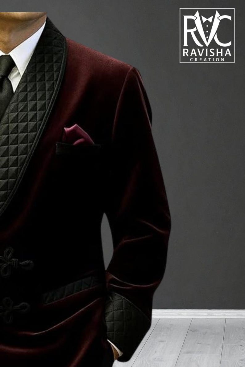 May include: A burgundy velvet blazer with black quilted lapels and cuffs. The blazer features a black tie, a white collared shirt, and a burgundy pocket square. The logo "RAVISHA CREATION" is visible in the upper right corner.