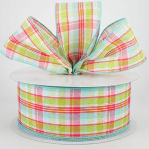 May include: A roll of plaid ribbon in shades of green, pink, yellow, and blue. The ribbon is arranged in a bow shape on top of the roll. The edges of the ribbon are trimmed with a light blue border.