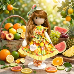 Puede incluir: Una muñeca de tela con largo cabello castaño, vestida con un vestido amarillo con estampado de naranjas y cítricos, un lazo a juego y medias a rayas naranjas y blancas. Una etiqueta en el vestido dice Michelle's Exclusive Handmade Doll.