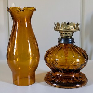May include: Amber-colored glass oil lamp with a matching ruffled shade. The lamp features a decorative base and a brass burner assembly. The shade is a flared shape. The lamp is designed for home decor.