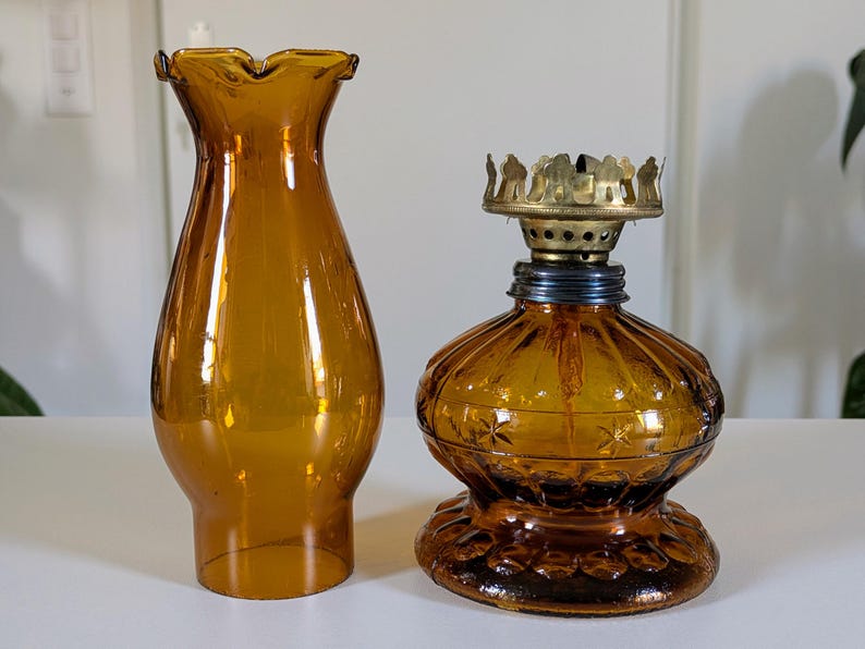 May include: Amber-colored glass oil lamp with a matching ruffled shade. The lamp features a decorative base and a brass burner assembly. The shade is a flared shape. The lamp is designed for home decor.