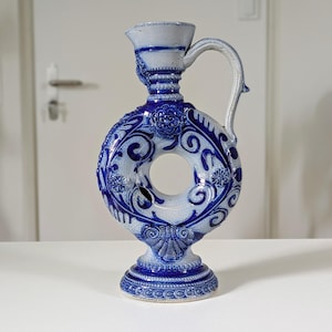 Peut inclure: Une cruche en céramique bleue et blanche avec un design circulaire unique. La cruche présente des motifs floraux complexes et une anse. La base est un piédestal et le dessus a un bec. La cruche est probablement à usage décoratif.