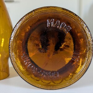 May include: Close-up of the bottom of a brown glass bottle. The base is circular with the embossed text "MADE IN HONG KONG" in a circular pattern. The bottle has a glossy, amber color.