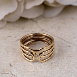 May include: A gold-colored ring with a unique open design. The ring features multiple parallel bands that curve around the finger, with an open space at the top. The ring's design is modern and geometric, suitable for everyday wear.