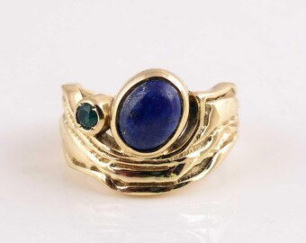 May include: A gold-toned ring featuring a large oval, deep blue gemstone and a smaller, round, green gemstone. The ring has a textured, organic design, with a flowing, sculpted appearance.