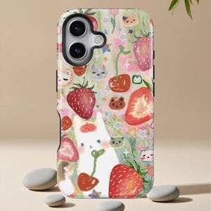 May include: A phone case with a whimsical design featuring strawberries, cats, and other cute illustrations. The case has a white background with a colorful pattern of red strawberries, green leaves, and various cartoon characters. The case is designed to fit a smartphone.