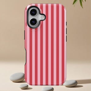May include: A pink and red striped phone case. The case has a black camera cutout and black side buttons. The case is shown with three small gray stones in front of it.