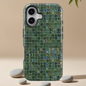 Puede incluir: Una funda de teléfono con estampado de mosaico verde. La funda presenta una cuadrícula de pequeñas baldosas cuadradas en tonos verdes, azules y amarillos. La funda del teléfono tiene una carcasa de cámara negra y botones laterales negros. La funda se muestra con tres piedras grises pequeñas y lisas.