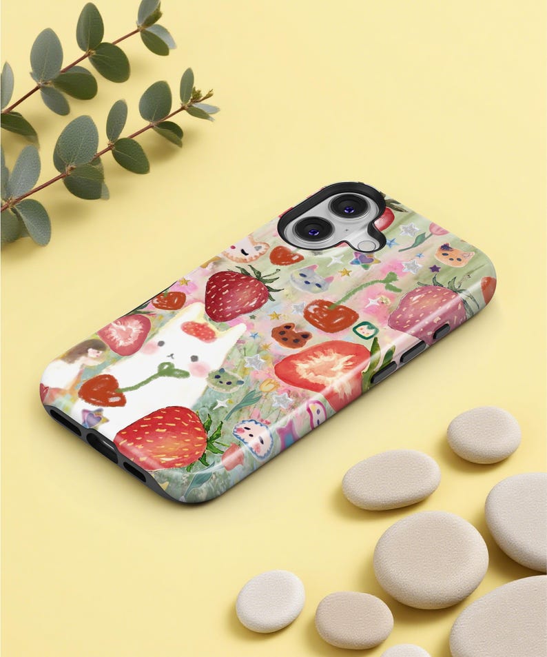 May include: A phone case with a whimsical design featuring strawberries, a white bunny, and other floral elements. The case has a glossy finish and a black border. The overall color scheme is pastel with red, pink, and green accents.