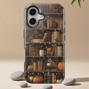 Puede incluir: Funda de teléfono con un diseño de estantería con calabazas, libros y luces de hadas. La funda tiene un borde transparente y una ilustración detallada de una escena de biblioteca con temática otoñal.