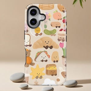 Può includere: Custodia per telefono beige con un motivo ripetuto di simpatiche illustrazioni di cibo, tra cui un croissant, un panino e un sole. La custodia ha un ritaglio nero per la fotocamera. Ci sono pietre grigie lisce in primo piano.